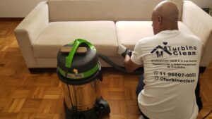Josué Barreto, supervisor técnico da Turbine Clean, fazendo a extração em um sofá bege com o equipamento profissional